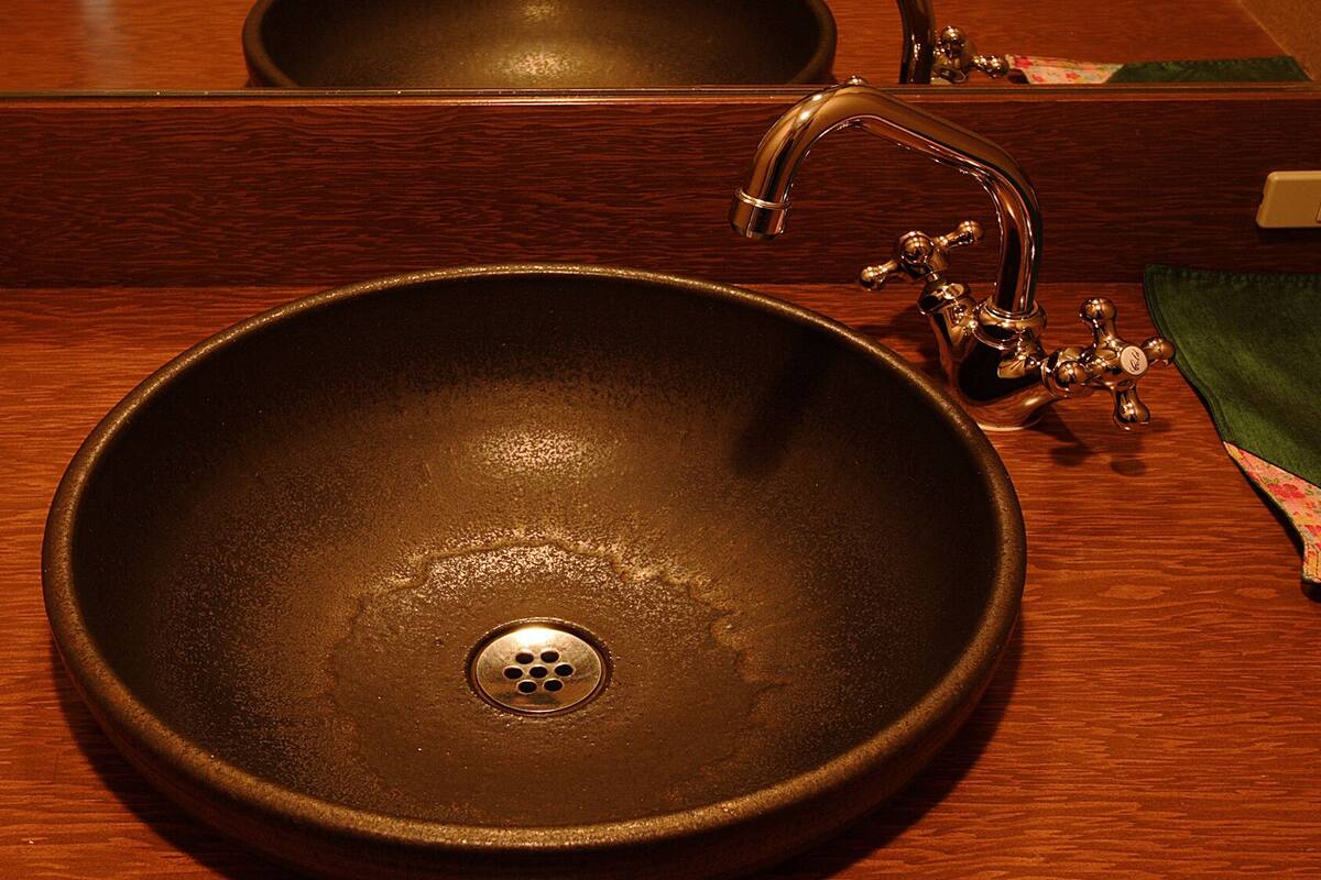 A round, dark-colored sink with a single drain, a faucet with a curved spout, and a mirror above it.
