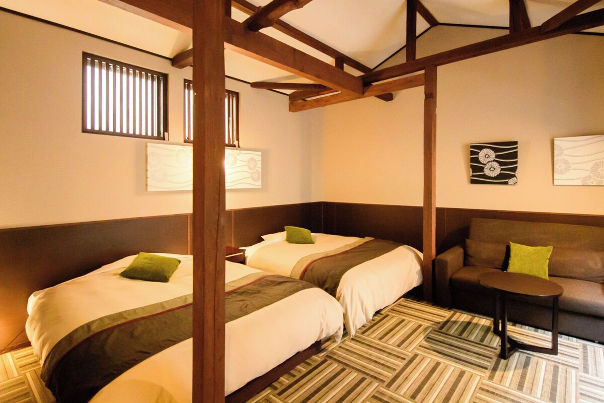 Habitación de hotel con dos camas, un sofá, una mesita y obras de arte en las paredes.