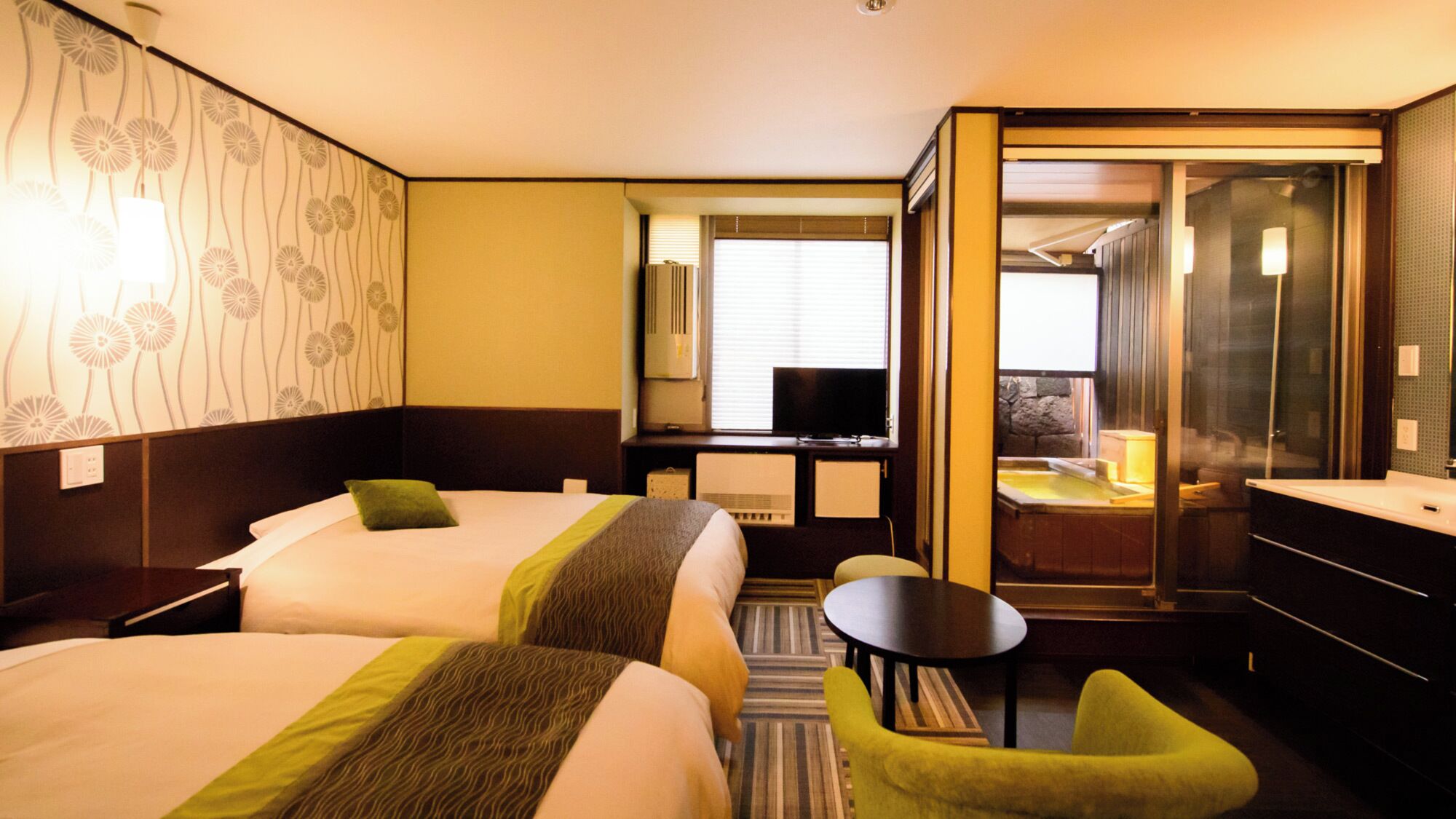 Ein Hotelzimmer mit zwei Betten, einem kleinen Tisch, einem Sessel, einem Fernseher und einem Badezimmer mit Badewanne.