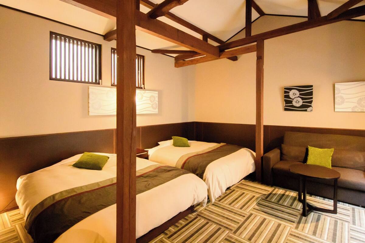 A hotel room with two beds, a sofa, a small table, and artwork on the walls.