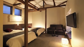 A room with two beds, a sofa, a TV, and a ceiling with wooden beams. - Kusatsu Onsen Yubatakesoan (Kusatsu)