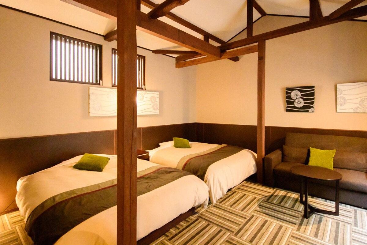 A hotel room with two beds, a sofa, a small table, and artwork on the walls.