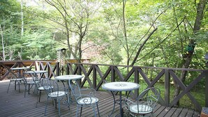 Une terrasse en bois, avec des tables et des chaises en métal, entourée d’arbres.