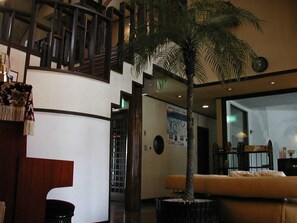 A lobby with a palm tree, a staircase, and a seating area. - Pension Cottage Shokubutsushi (Hakuba)