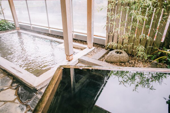 A tranquil indoor water feature with stone tiles, wooden beams, and bamboo plants.