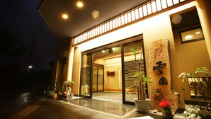 A hotel entrance with a wet pavement, potted plants, and a traditional Asian-style wall decoration.