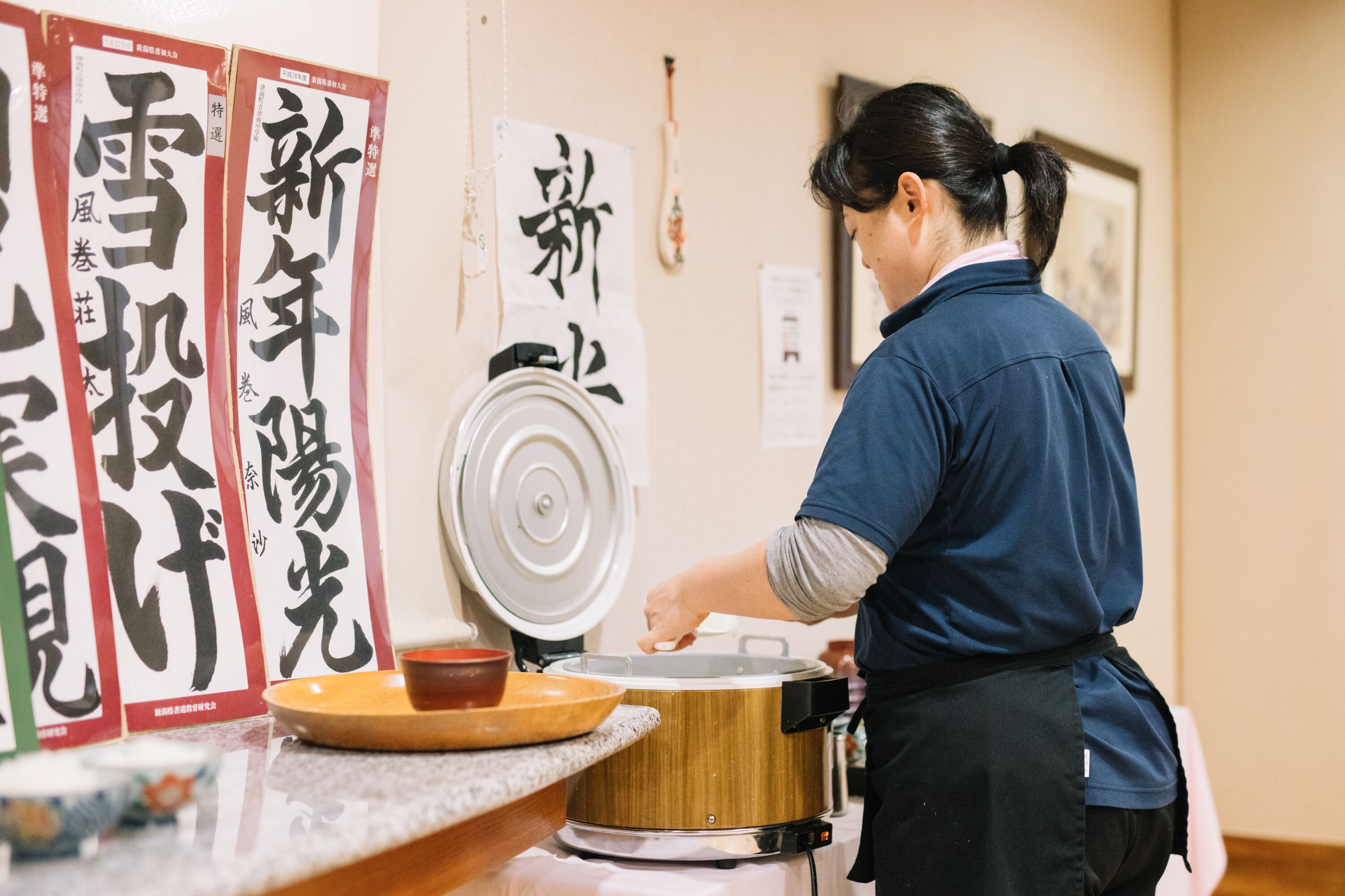A person cooking in a kitchen with a rice cooker and a wooden table.