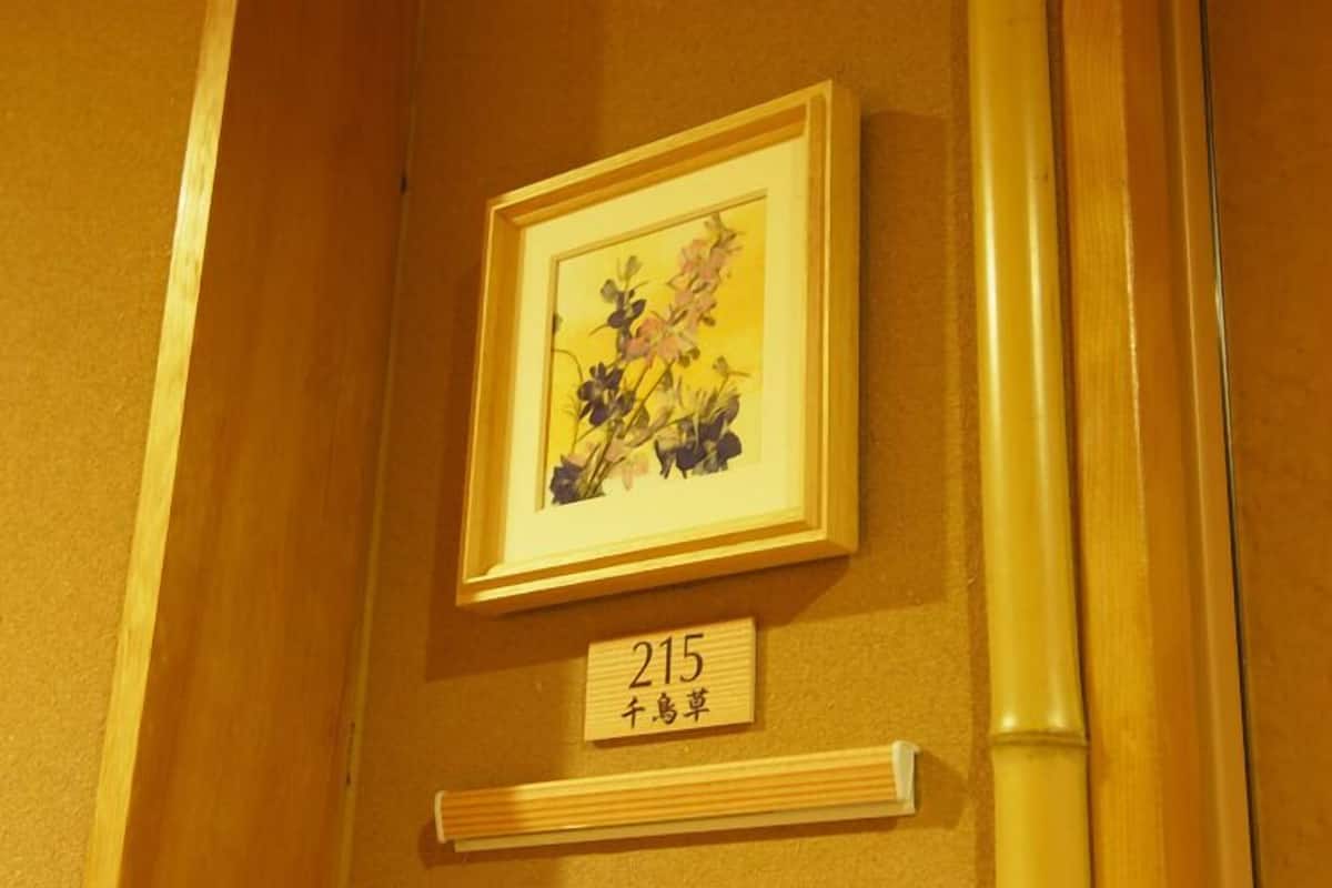 Ein gerahmtes Bild mit Blumen an einer Wand, darunter ein Schild mit einer Zimmernummer.