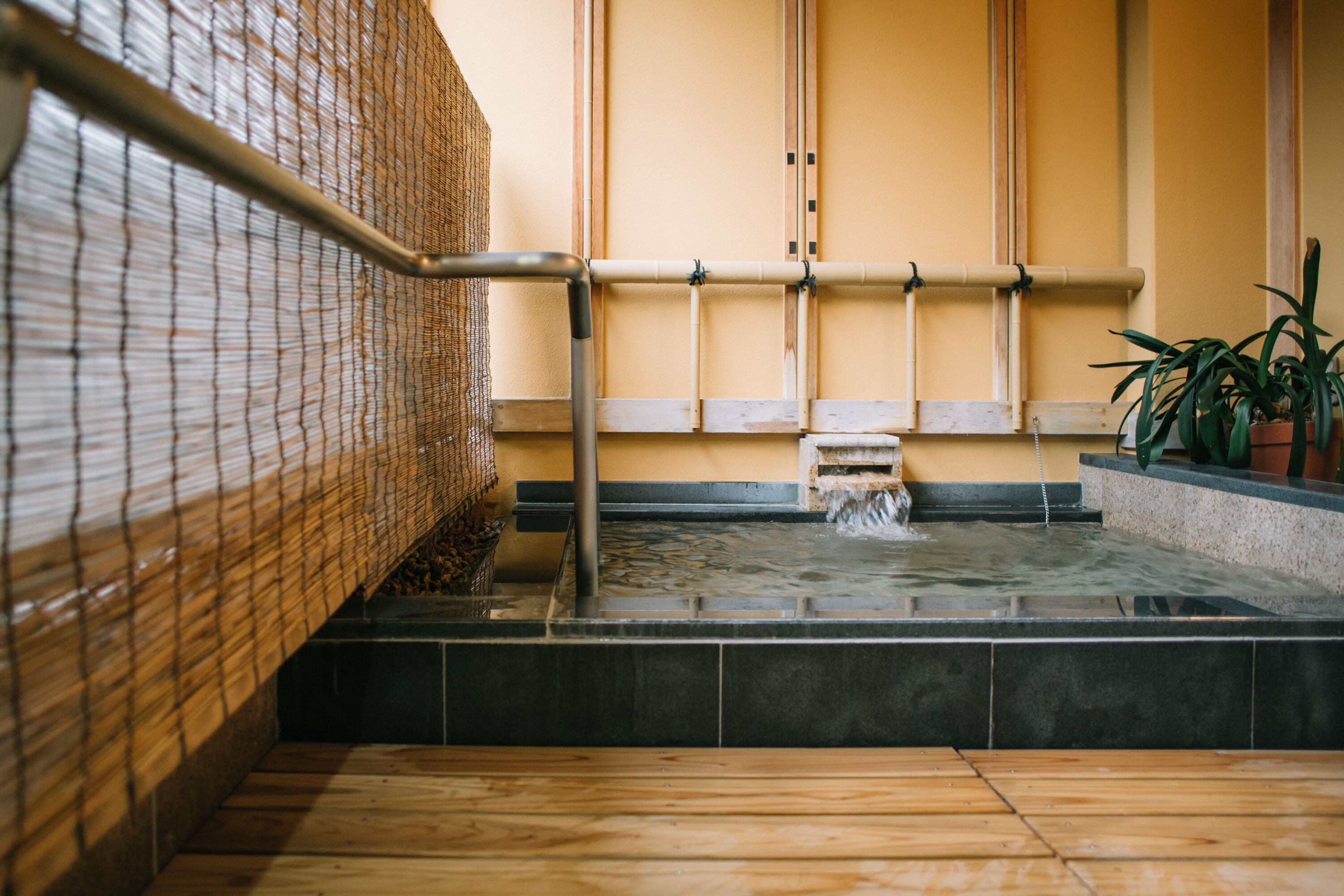 Un onsen japonais traditionnel, avec un plancher en bois, des rampes en bambou et un espace de baignade en pierre.