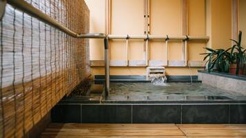 Un onsen japonais traditionnel, avec un plancher en bois, des rampes en bambou et un espace de baignade en pierre.