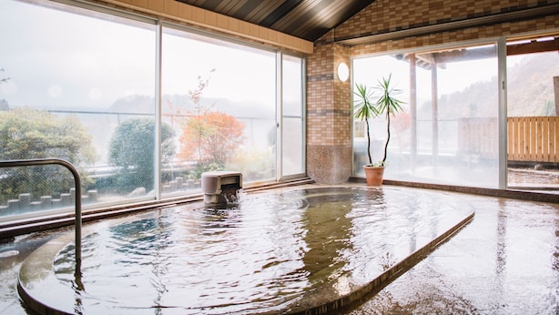 A hot tub with a view of a bridge and trees, surrounded by large windows and a tiled floor.