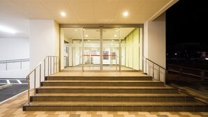 A building entrance with a set of stairs leading to a glass door, a sign above the door, and a parking area to the left. - Hotel Sunroute Sukagawa (Sukagawa)