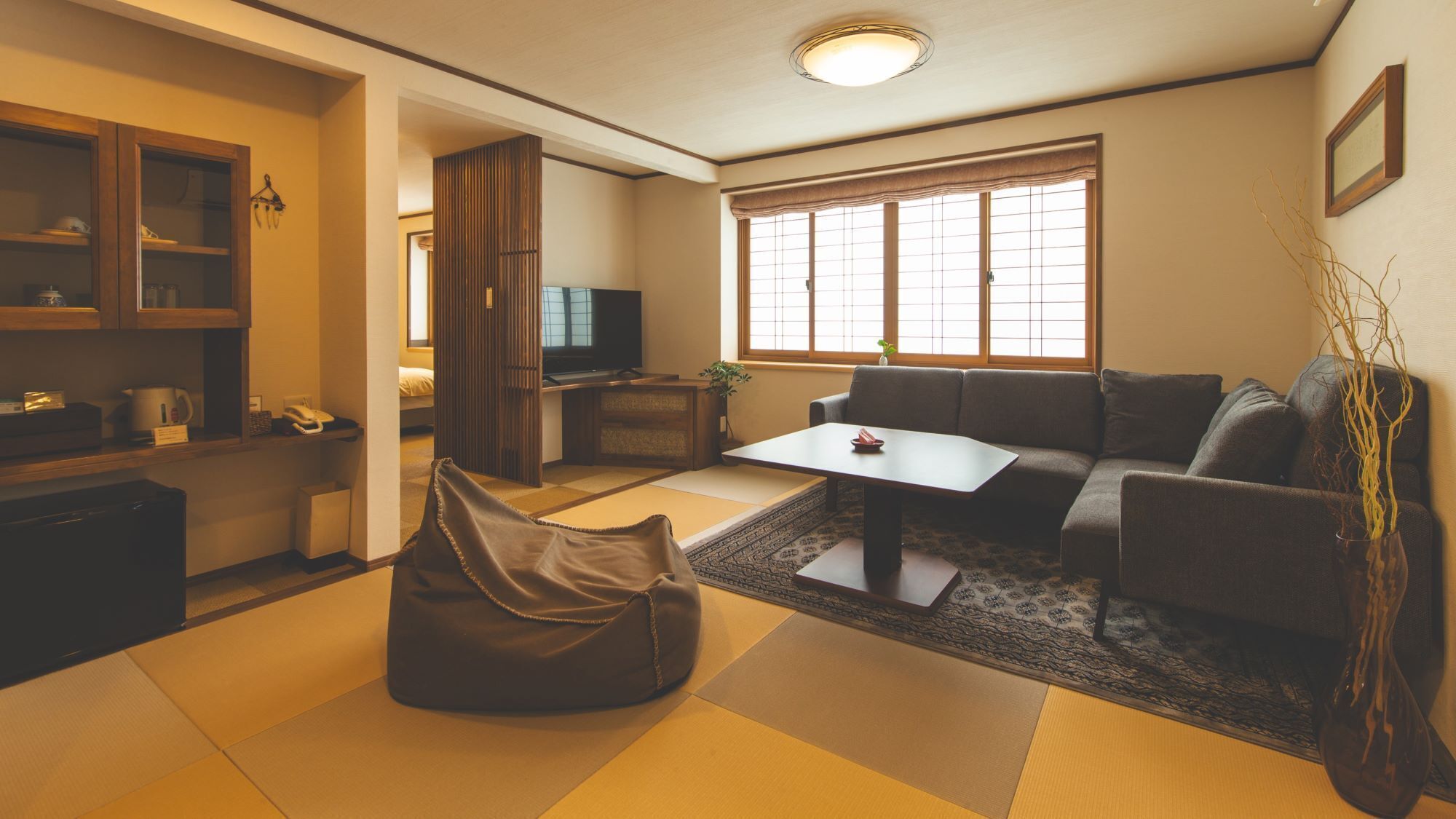 Ein Wohnzimmer mit Tatami-Matten, einer Couch, einem Couchtisch, einem Fernseher und einer Vitrine mit Glastüren.