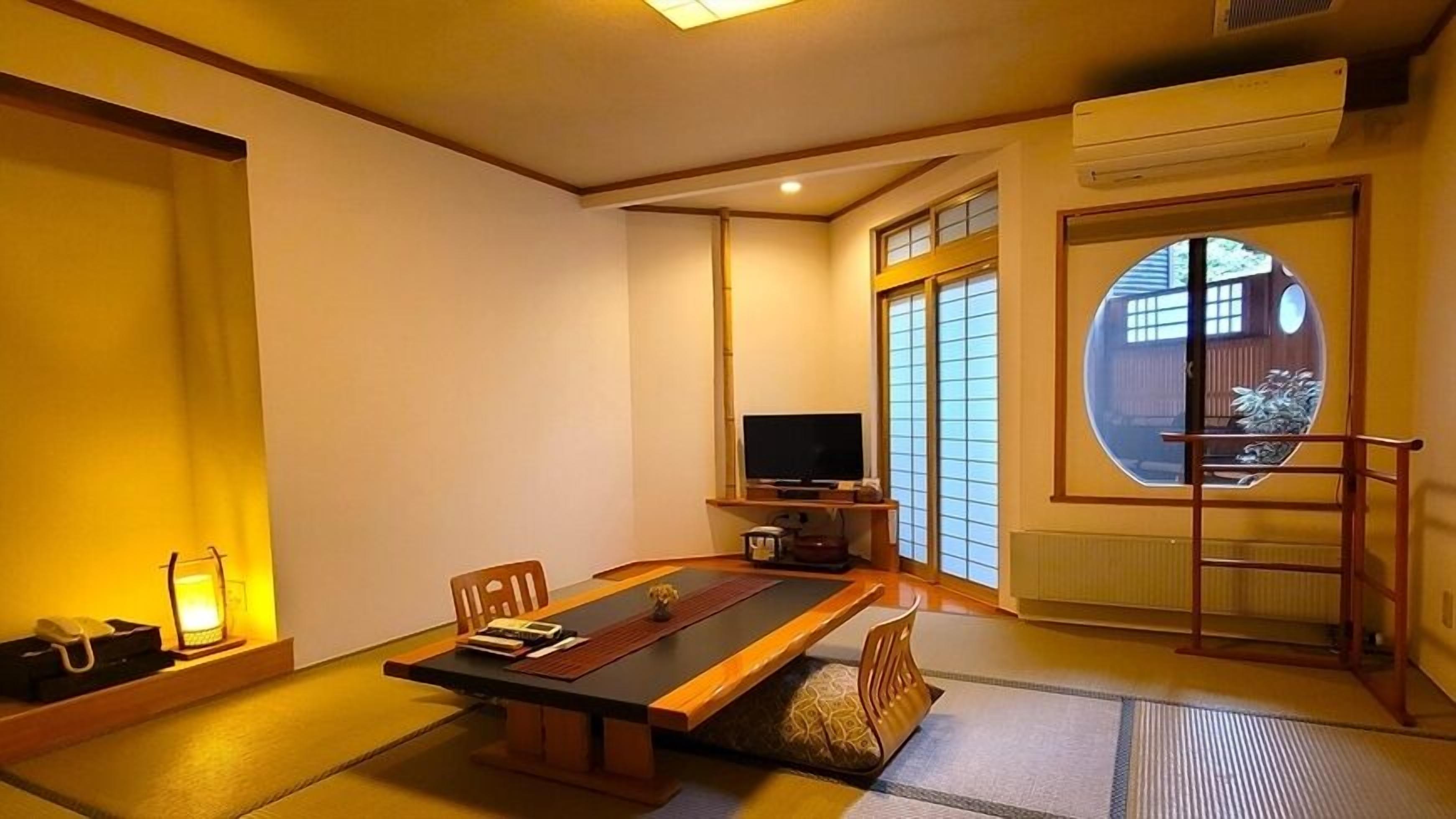 Habitació japonesa tradicional amb sòls de tatami, una taula baixa, televisió i una porta corredissa que dona a un balcó.