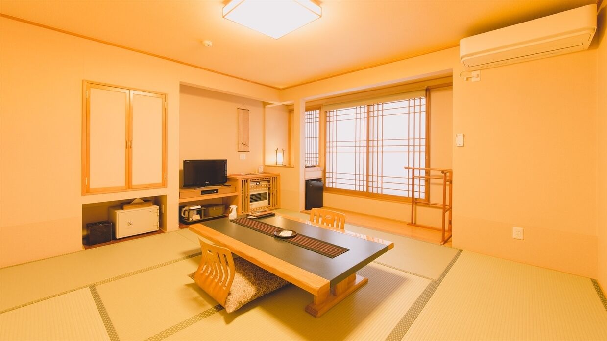Habitació japonesa tradicional amb sòl de tatami, una taula baixa, cadirees, televisió i finestra amb un disseny de reixa.