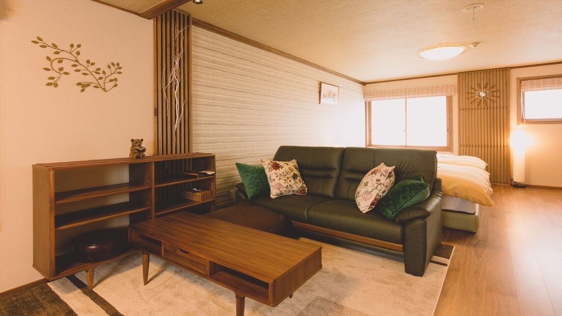 Ein Wohnzimmer mit einer Couch, einem Holztisch, einem Bücherregal und einem Fenster mit Jalousien.