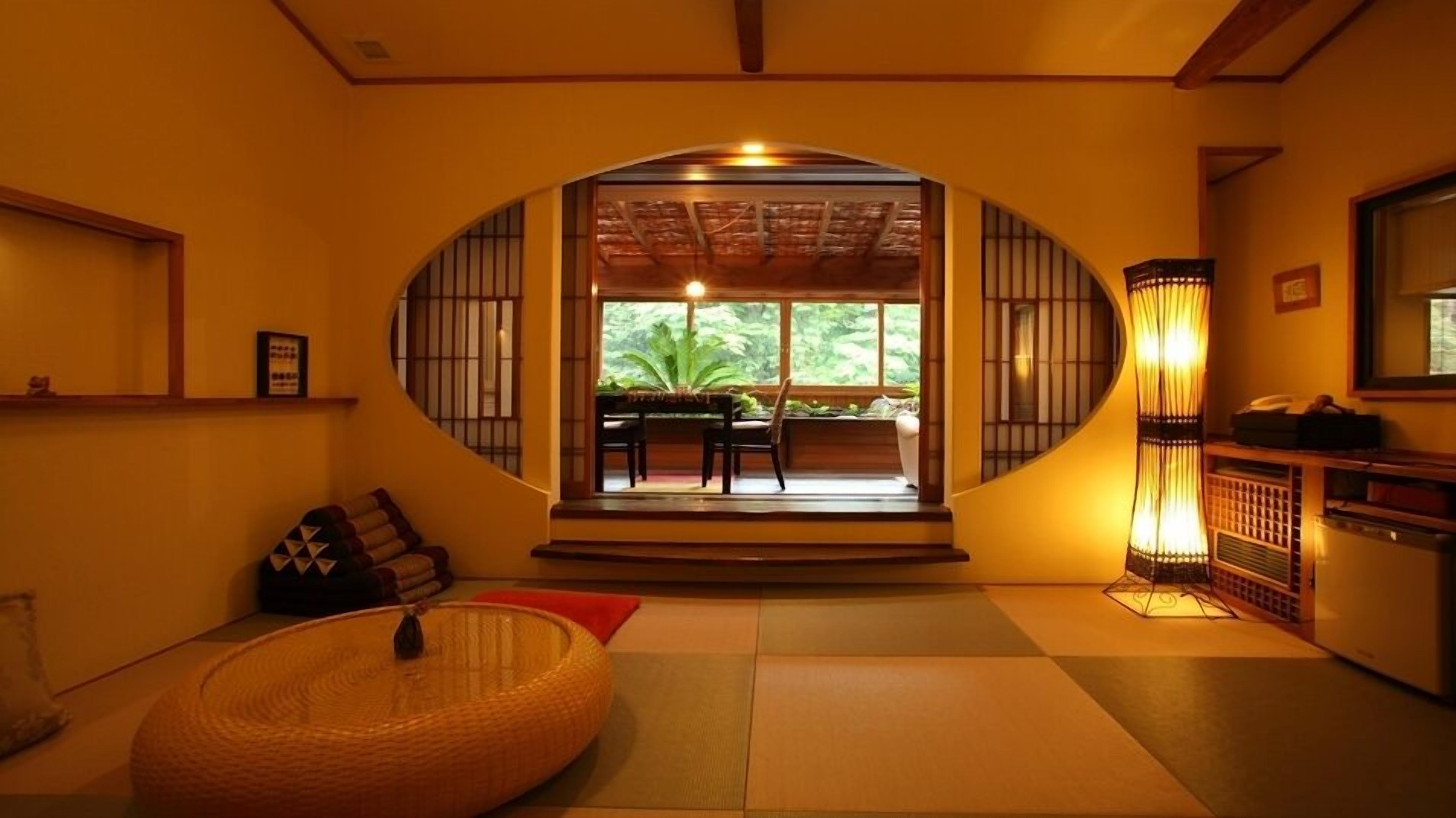 Ein traditionelles japanisches Interieur mit Tatami-Böden, einem niedrigen Tisch mit Stühlen und einem großen Fenster mit Blick auf Grünflächen.