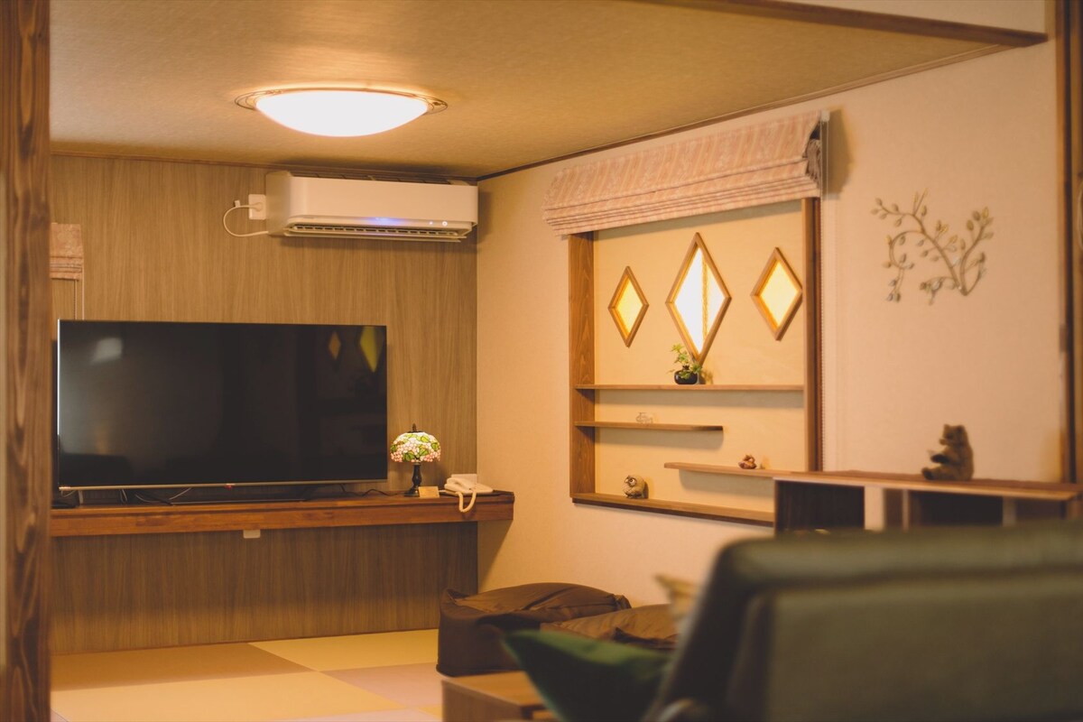 A living room with a flat-screen TV, a lamp, a sofa, and a wall-mounted air conditioner.