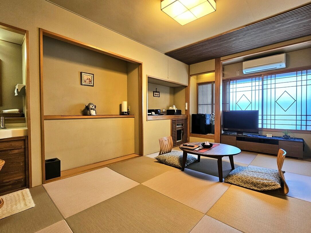 Una habitació japonesa tradicional amb fons de tatami, una taula baixa, televisió i portes corredisses.