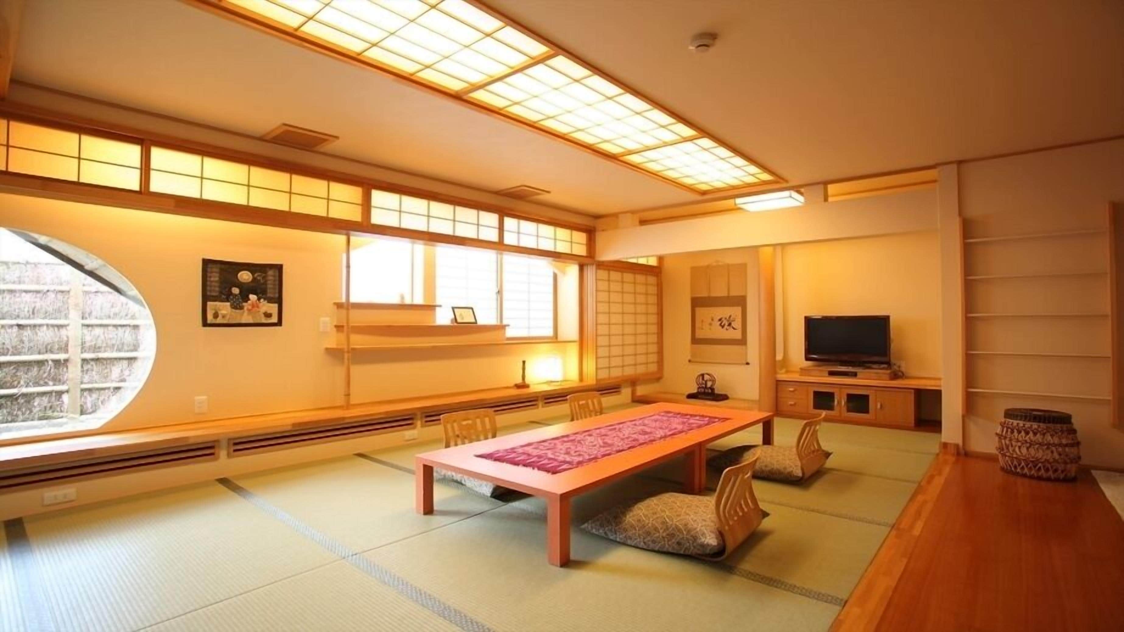 Una habitació japonesa tradicional amb tatami, una taula baixa amb un estriat rosa, una televisió i portes corredisses.