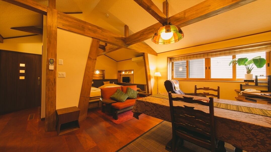 Ein Zimmer mit Holzboden, einem Bett mit Kissen, einem Tisch mit Stühlen und einem Fenster mit Pflanze.