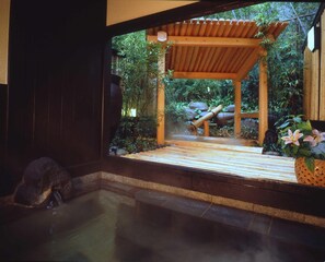 A traditional Japanese onsen with a wooden structure, a stone bath, and lush greenery. - Hana No Omotenashi Nanraku (Minamiizu)