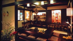A traditional Japanese-style room with tatami mats, a low table with a tea set, and shelves with ceramics and textiles. - Hana No Omotenashi Nanraku (Minamiizu)