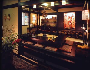 A traditional Japanese-style room with tatami mats, a low table with a tea set, and shelves with ceramics and textiles. - Hana No Omotenashi Nanraku (Minamiizu)