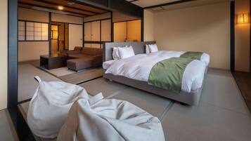 A modern hotel room with a large bed, a sofa, and a seating area with cushions.