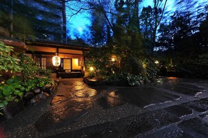 Un edificio japonés tradicional con fachada de madera, un camino de piedra que conduce a la entrada y un letrero con caracteres japoneses.