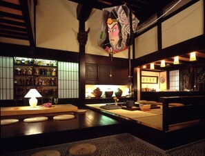 A traditional Japanese interior with tatami flooring, a low wooden table, a hanging decorative item, and a shelf with glassware. - Hana No Omotenashi Nanraku (Minamiizu)
