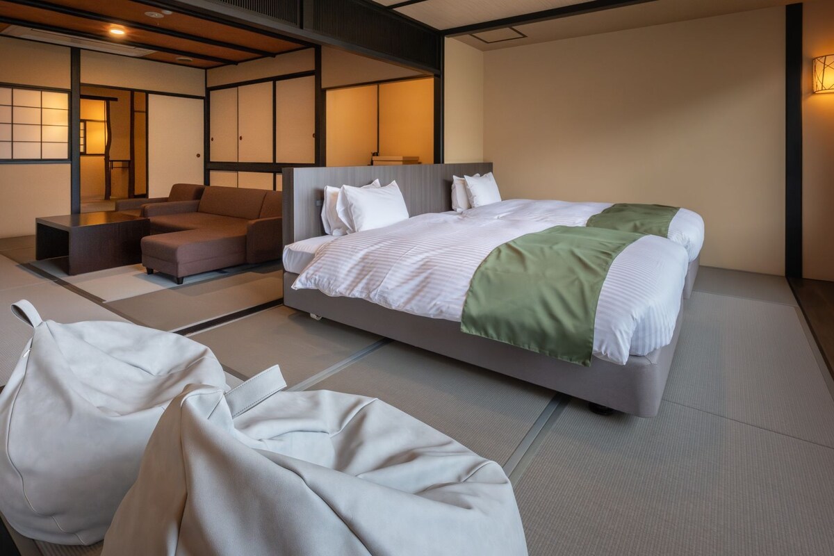 A modern hotel room with a bed, seating area, and traditional tatami flooring.