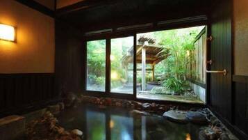 A traditional Japanese room with tatami flooring, a stone water feature, and a view of a garden through a sliding door.