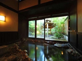 Una habitación japonesa tradicional con suelo de tatami, una fuente de agua de piedra y vistas a un jardín a través de una puerta corredera.