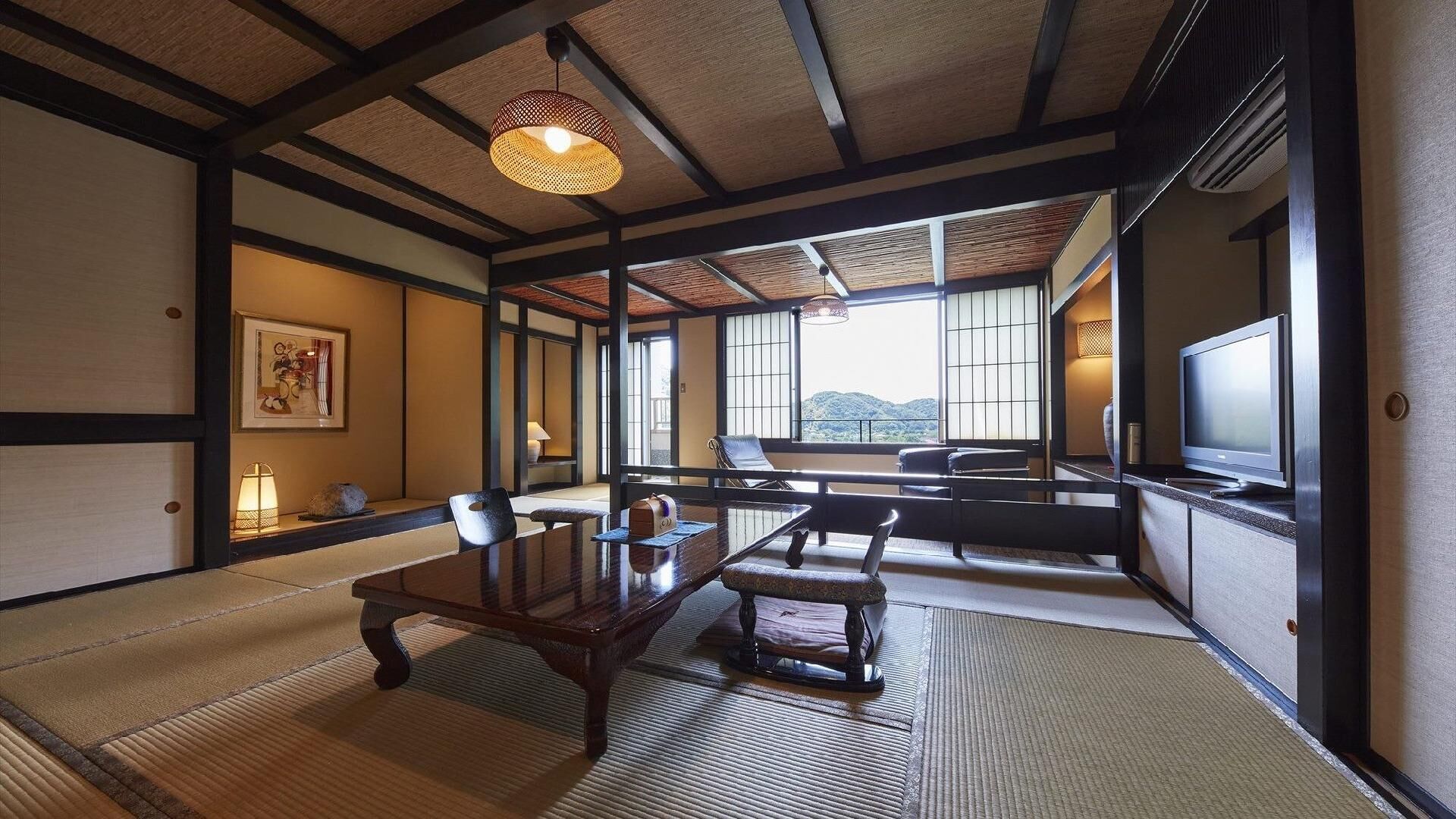 Une pièce de style japonais traditionnel, avec un sol recouvert de tatamis, une table basse, des chaises, un téléviseur et de grandes fenêtres donnant sur l’extérieur.