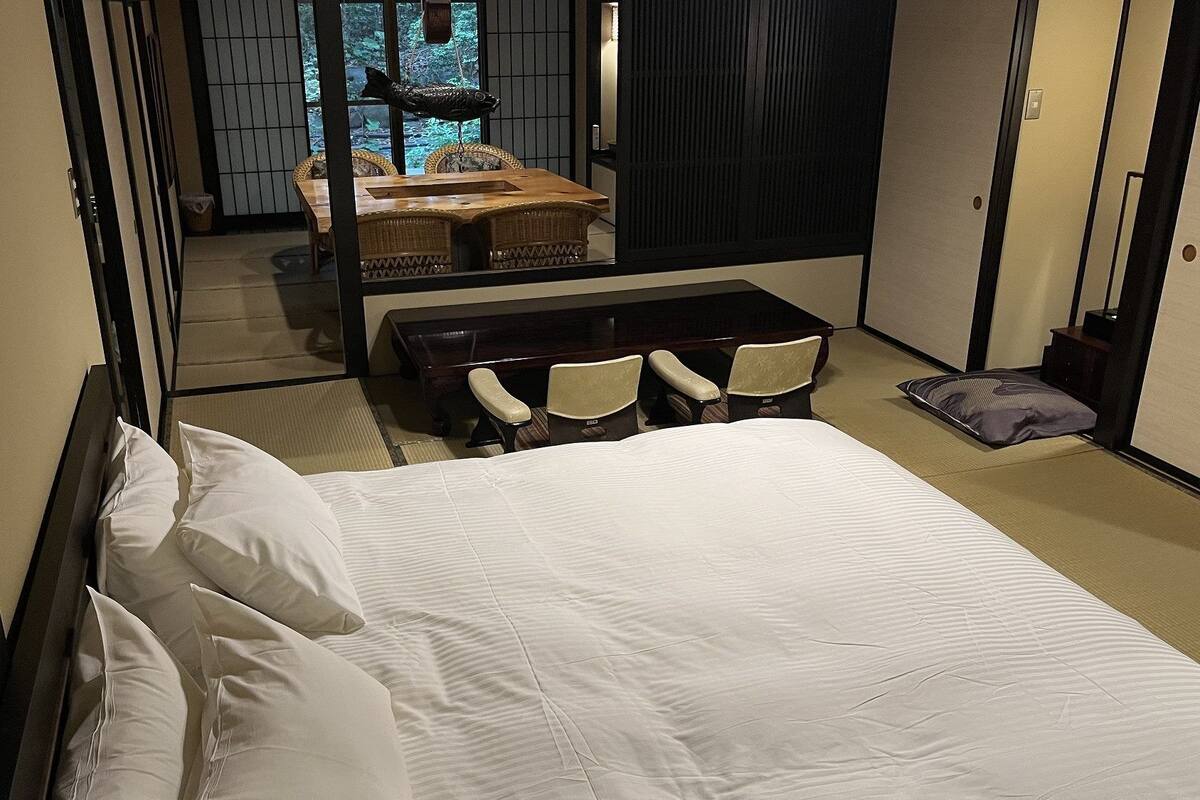 Ein Hotelzimmer mit einem Bett, einem kleinen Tisch, zwei Stühlen, einem Sofa und Blick auf einen Wald durch ein Fenster.