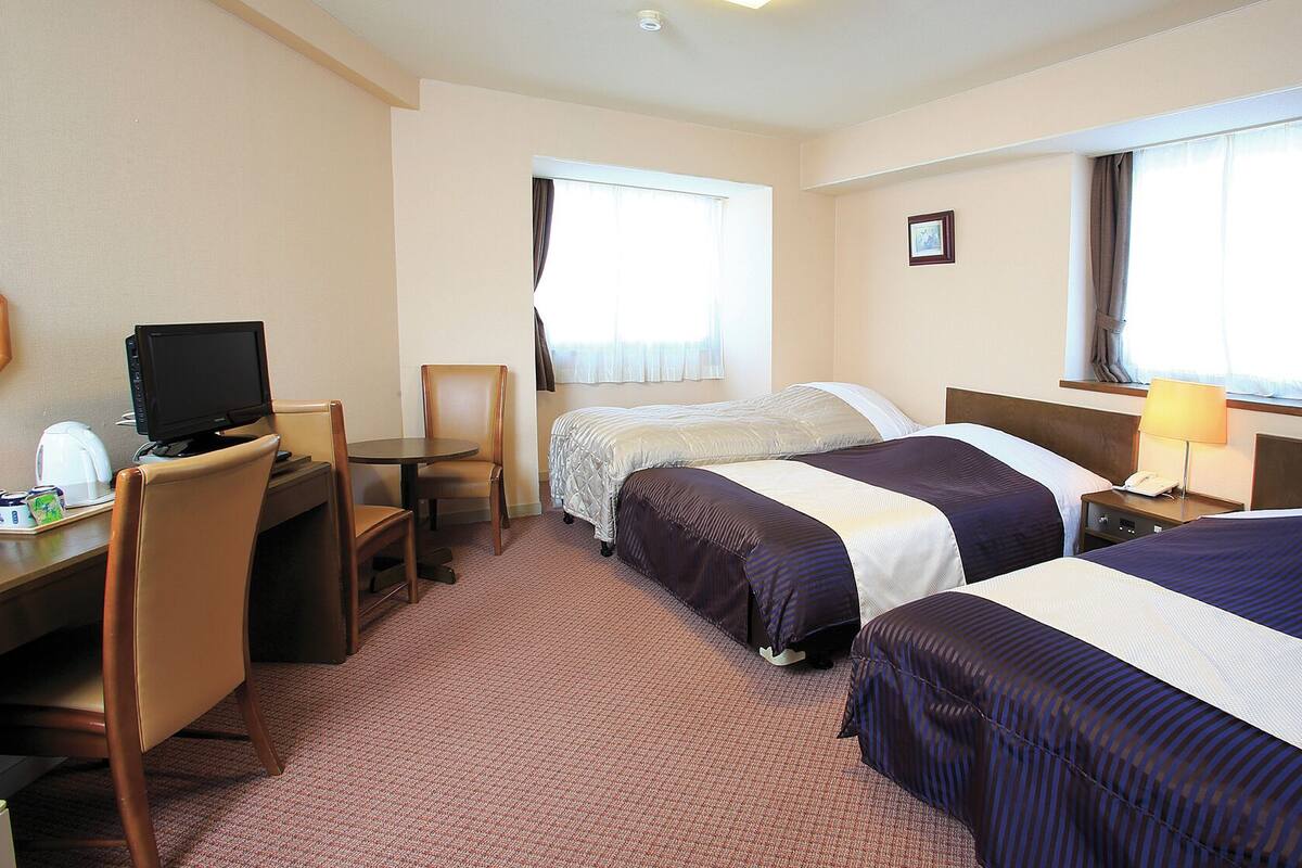 A hotel room with two beds, a desk with a computer, a chair, and a window with curtains.