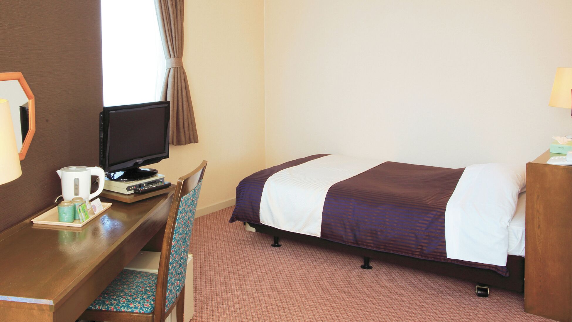 A hotel room with a bed, a desk with a television, a coffee maker, and a chair.