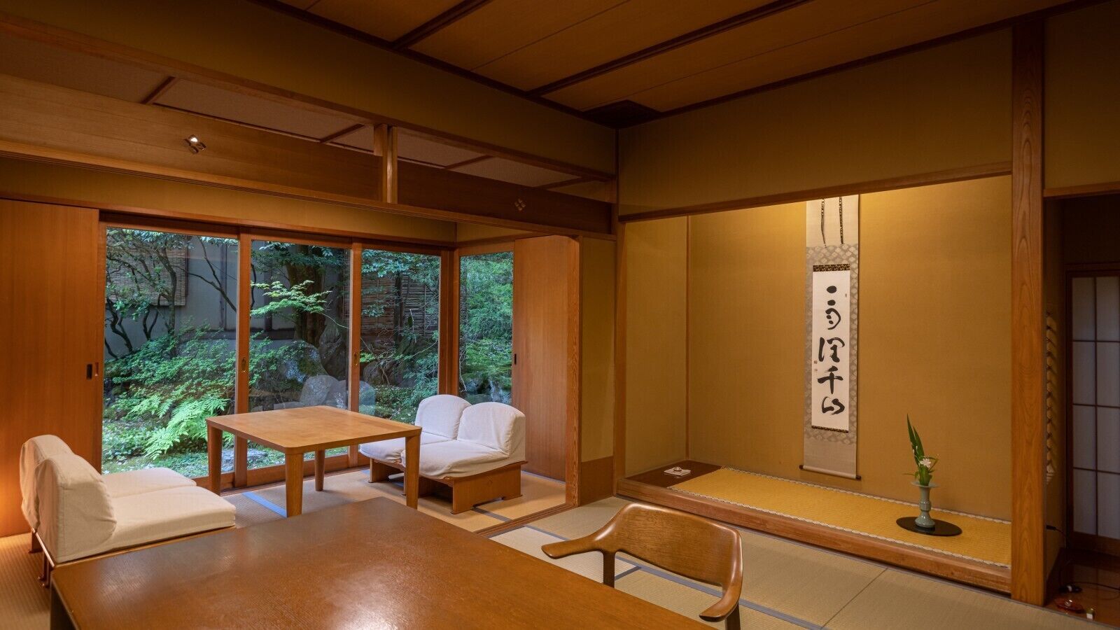 Une pièce de style japonais traditionnel, avec un sol recouvert de tatamis, une table basse, un canapé et une porte coulissante donnant sur un jardin.
