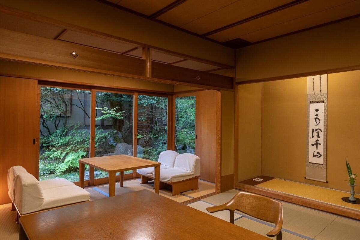 A traditional Japanese room with tatami flooring, a low table, a sofa, and a sliding door leading to a garden.
