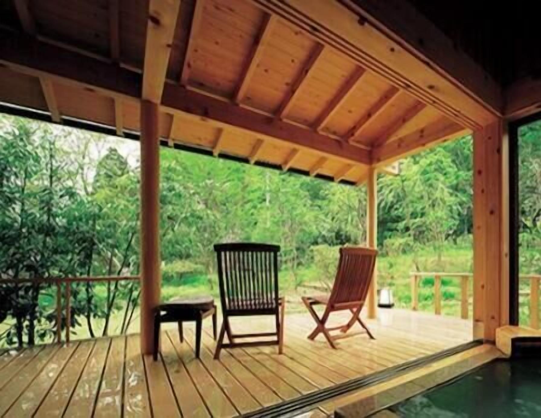 A wooden deck with two chairs and a small table, surrounded by lush greenery.