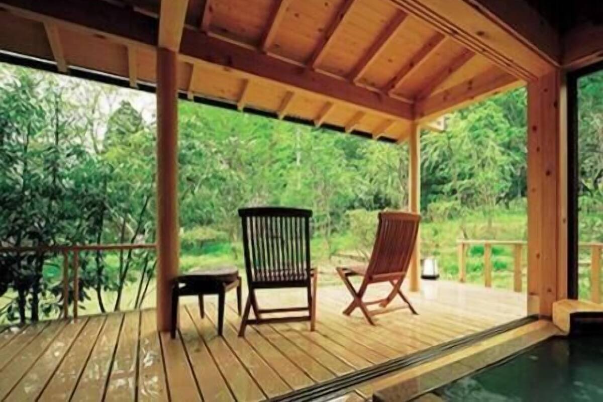 A wooden deck with two chairs and a small table, surrounded by lush greenery.