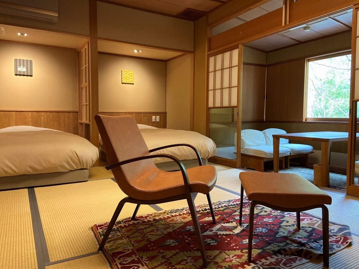 A room with two beds, a chair, a table, and a window.