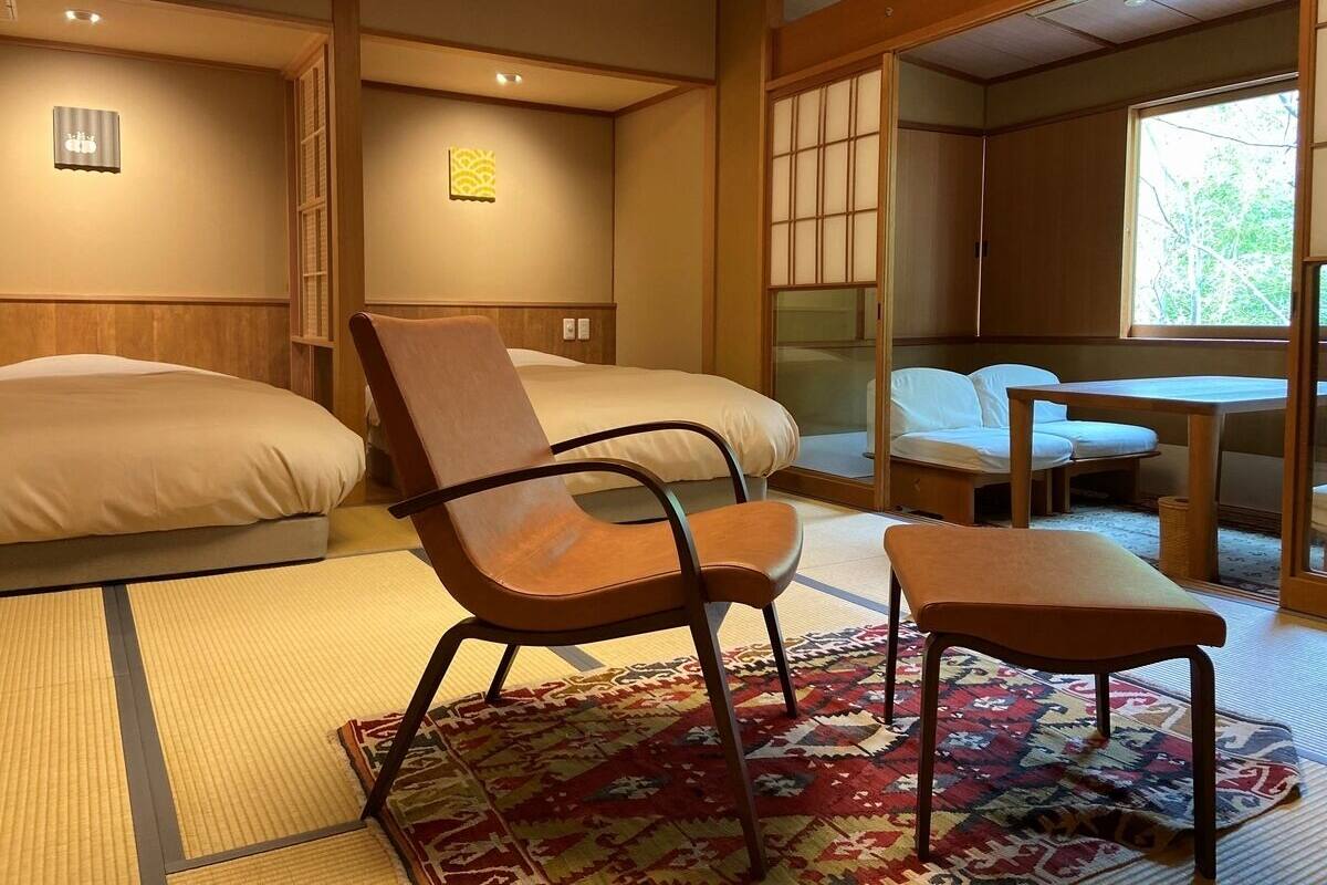 A room with two beds, a chair, a table, and a window.