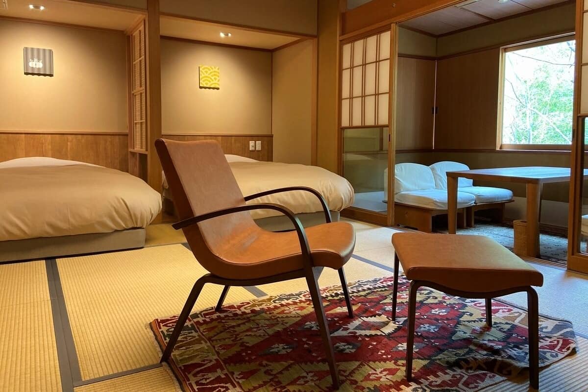 A room with two beds, a chair, a table, and a window.