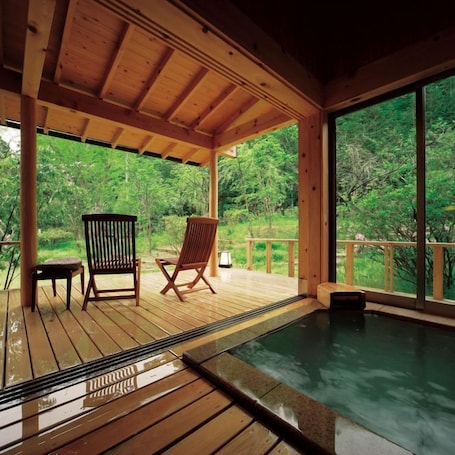 A wooden deck with a hot tub, two wooden chairs, and a view of a forest.