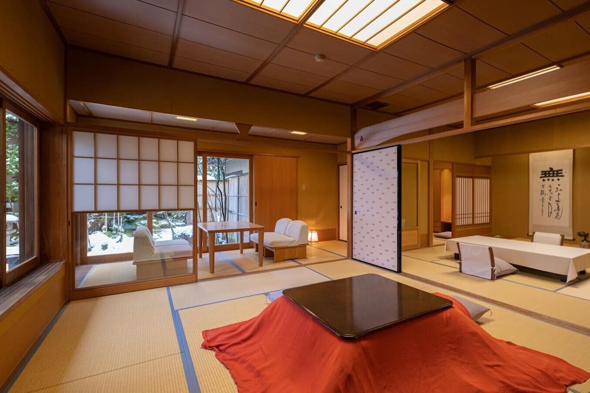 A traditional Japanese room with tatami flooring, a tatami mat table, a low wooden table, sliding doors, and a view through a window.