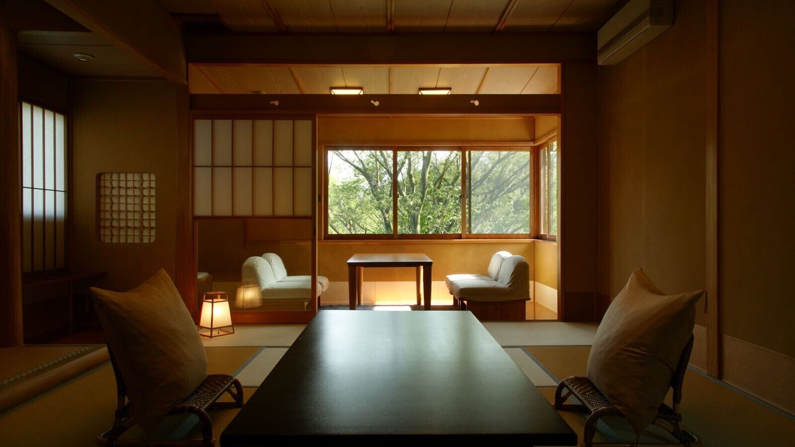A traditional Japanese room with tatami flooring, a low table, two chairs, and a large window with a view of trees.