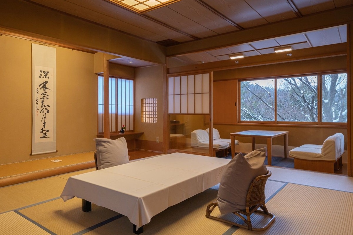 Une pièce de style japonais traditionnel, avec un sol recouvert de tatamis, une table basse, un lit et des portes coulissantes.