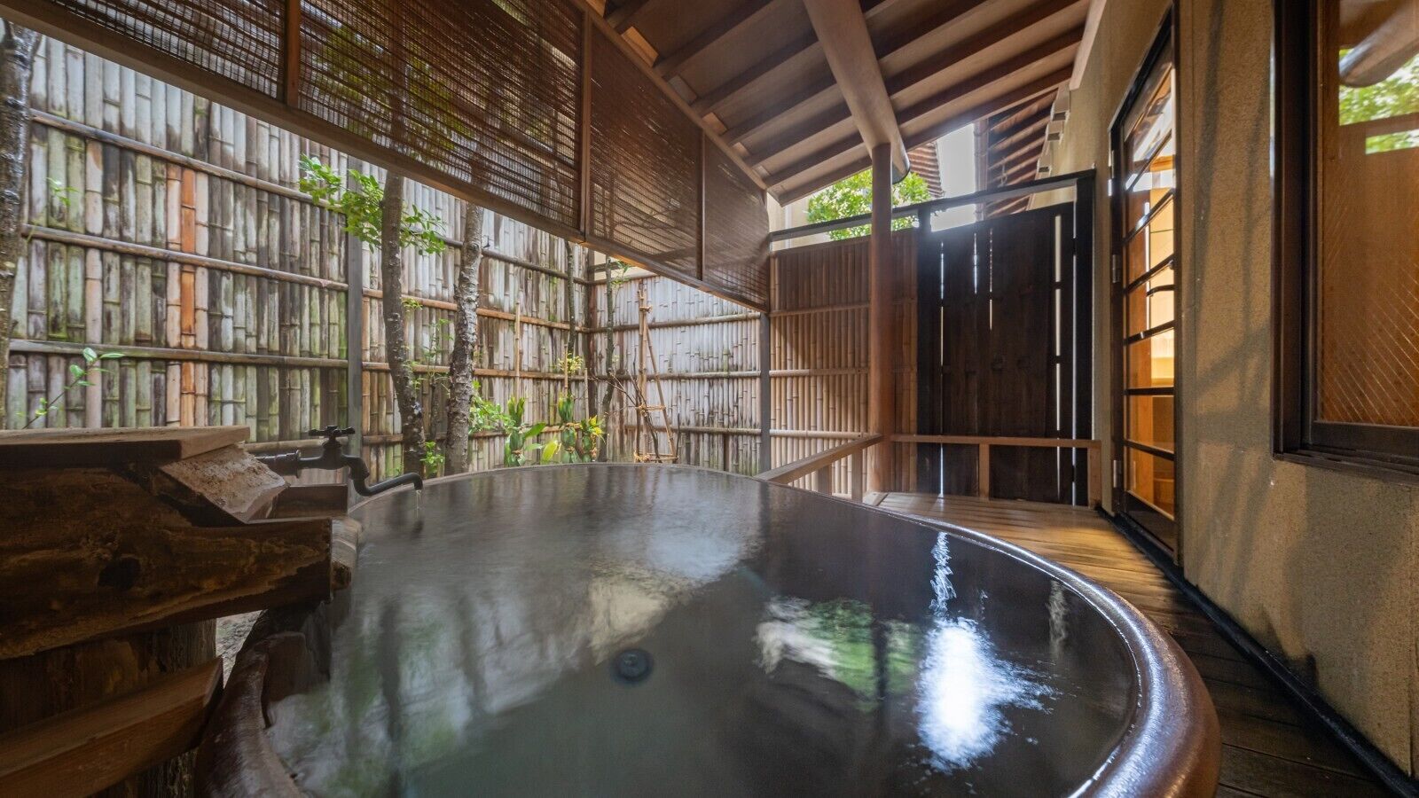 A traditional Japanese onsen with a wooden interior, a hot spring bath, and a bamboo fence.
